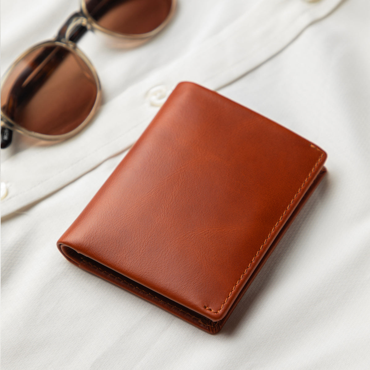 Brown leather wallet on a white surface with sunglasses in the background
